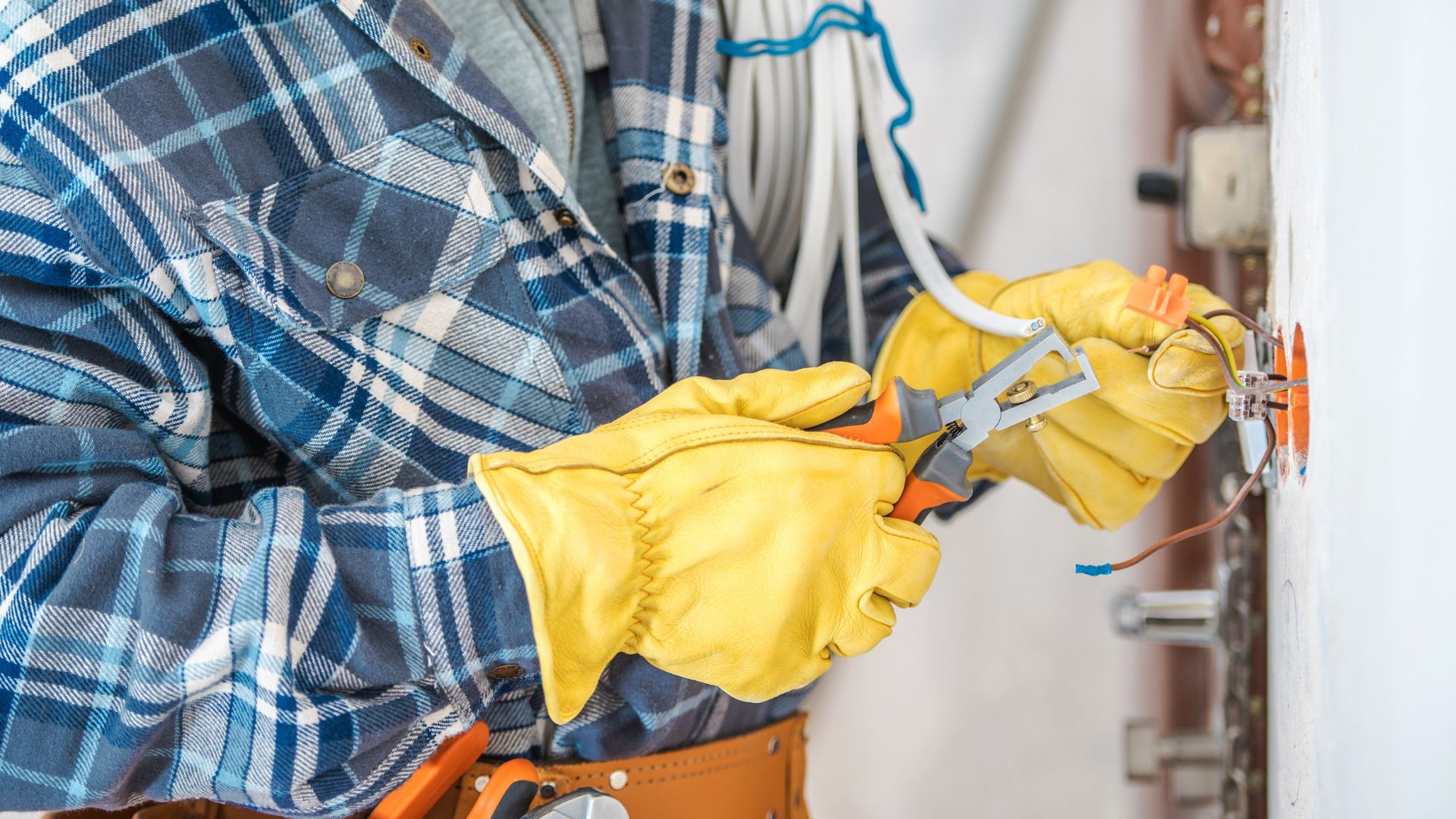 Gloved electrician stripping and terminating wires at a wall outlet during an inspection
